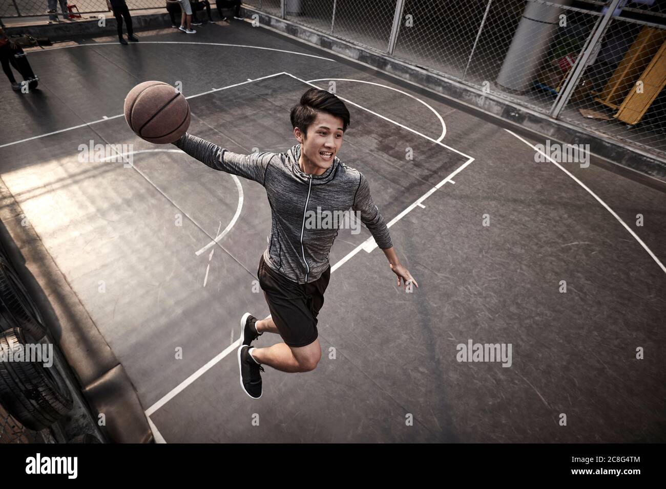jeune asiatique adulte homme joueur de basket-ball essayant une dunk slam sur le terrain extérieur Banque D'Images