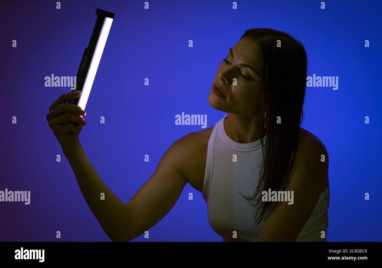 La jeune femme tient une lampe LED sur fond bleu. Modèle femelle lors de la présentation de l'éclairage LED de Nanlite Studio. Coulisses. Juin 2020, Kiev Ukraine Banque D'Images