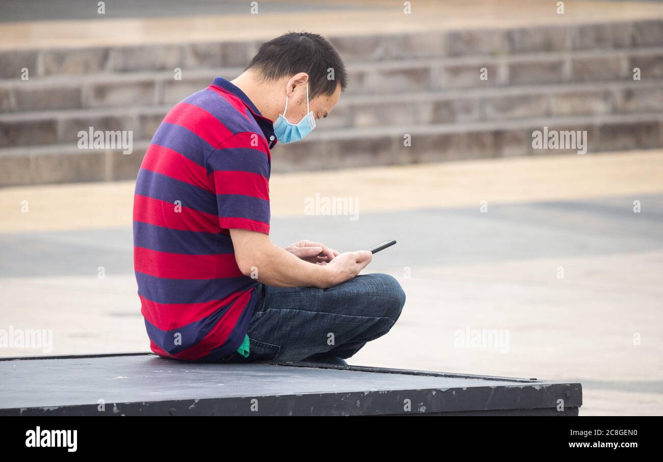 Homme asiatique portant le visage homme couvrant regardant le téléphone mobile. Banque D'Images