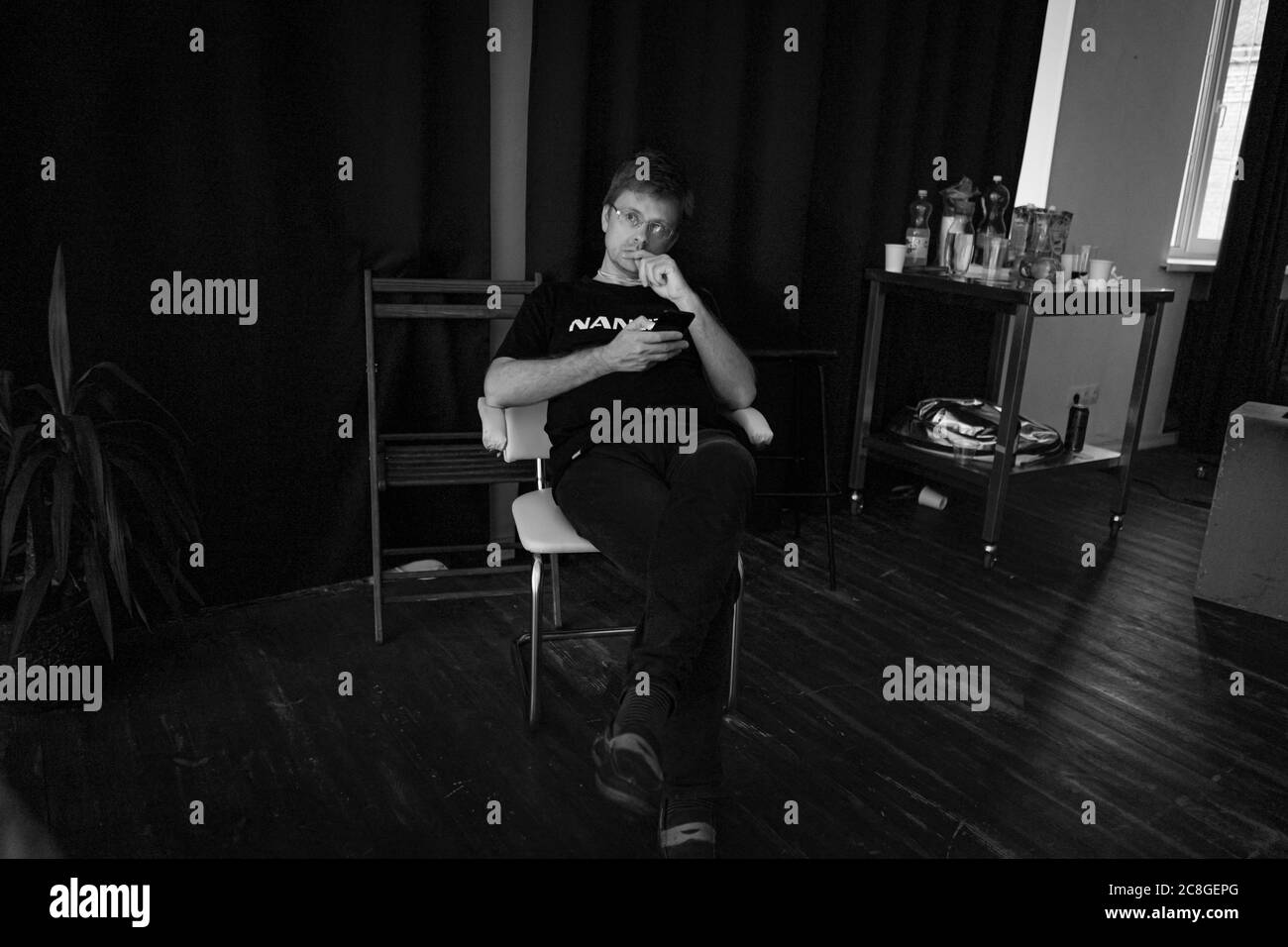 L'homme pensif utilise le téléphone assis en studio sur fond noir. Présentation de l'éclairage LED de Nanlite Studio. Coulisses de la présentation. Juin 2020, Kiev Banque D'Images