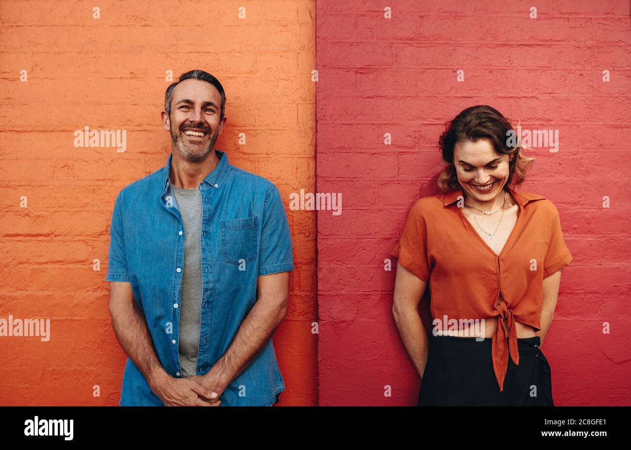 Homme et femme debout sur un mur rouge et orange. Couple se penchant sur un mur coloré et souriant. Banque D'Images