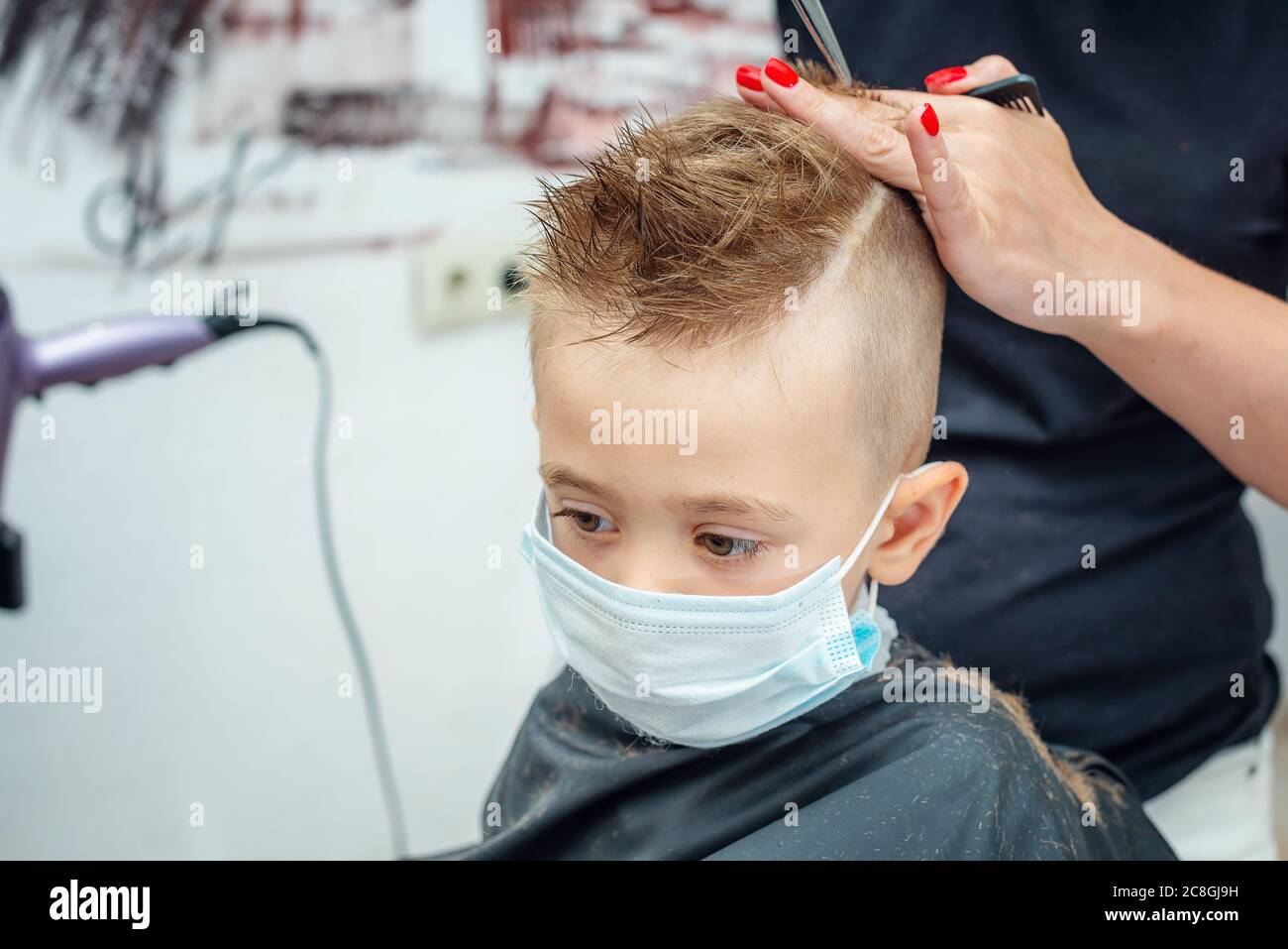 Nouveau normal s'adaptant à la vie normale après un blocage pandémique. Garçon se couper les cheveux portant un masque. Banque D'Images