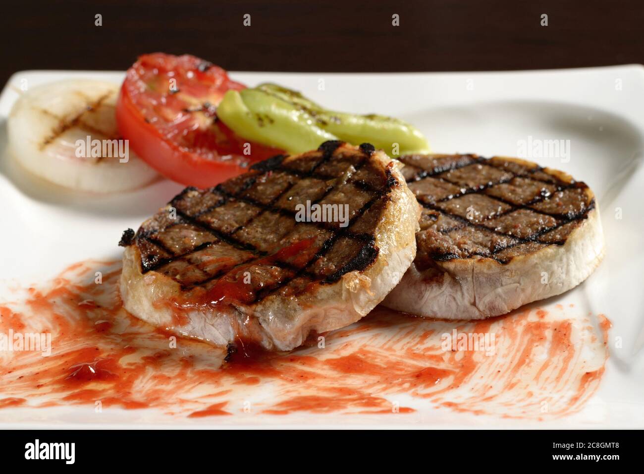 Deux côtelettes de bœuf grillées sur l'assiette en gros plan avec des légumes grillés de tomate, d'oignon et de poivron. Photos pour les menus du restaurant et du café Banque D'Images