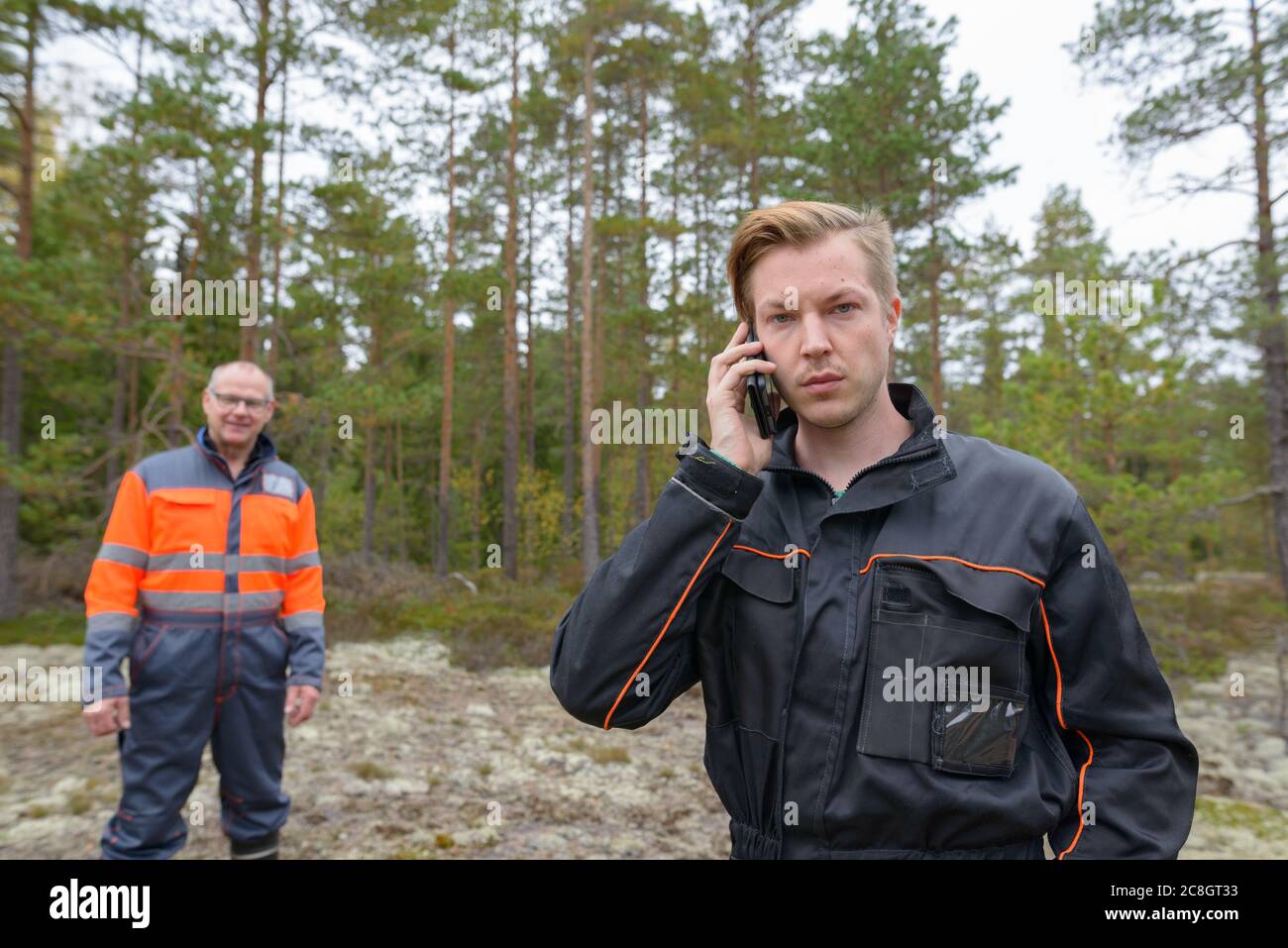 Jeune homme parlant sur téléphone mobile dans la forêt avec heureux homme mature dans le fond Banque D'Images