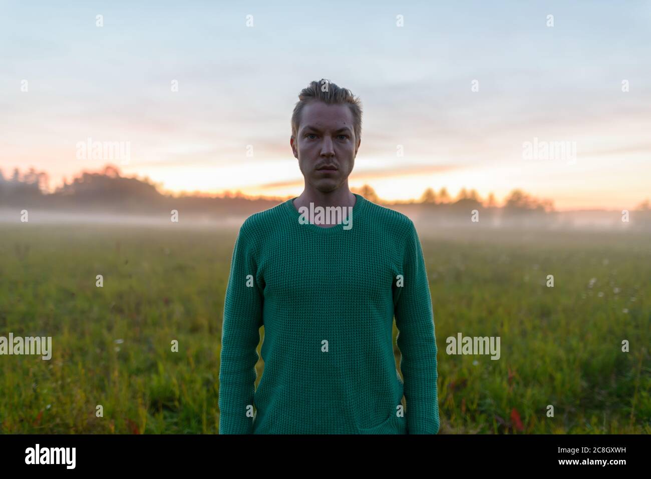 Jeune homme beau contre le champ d'herbe avec brouillard à la fin de l'aube Banque D'Images