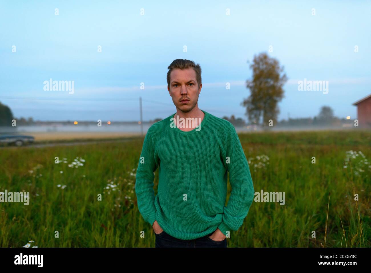 Jeune homme beau contre le champ d'herbe avec brouillard à la fin de l'aube Banque D'Images