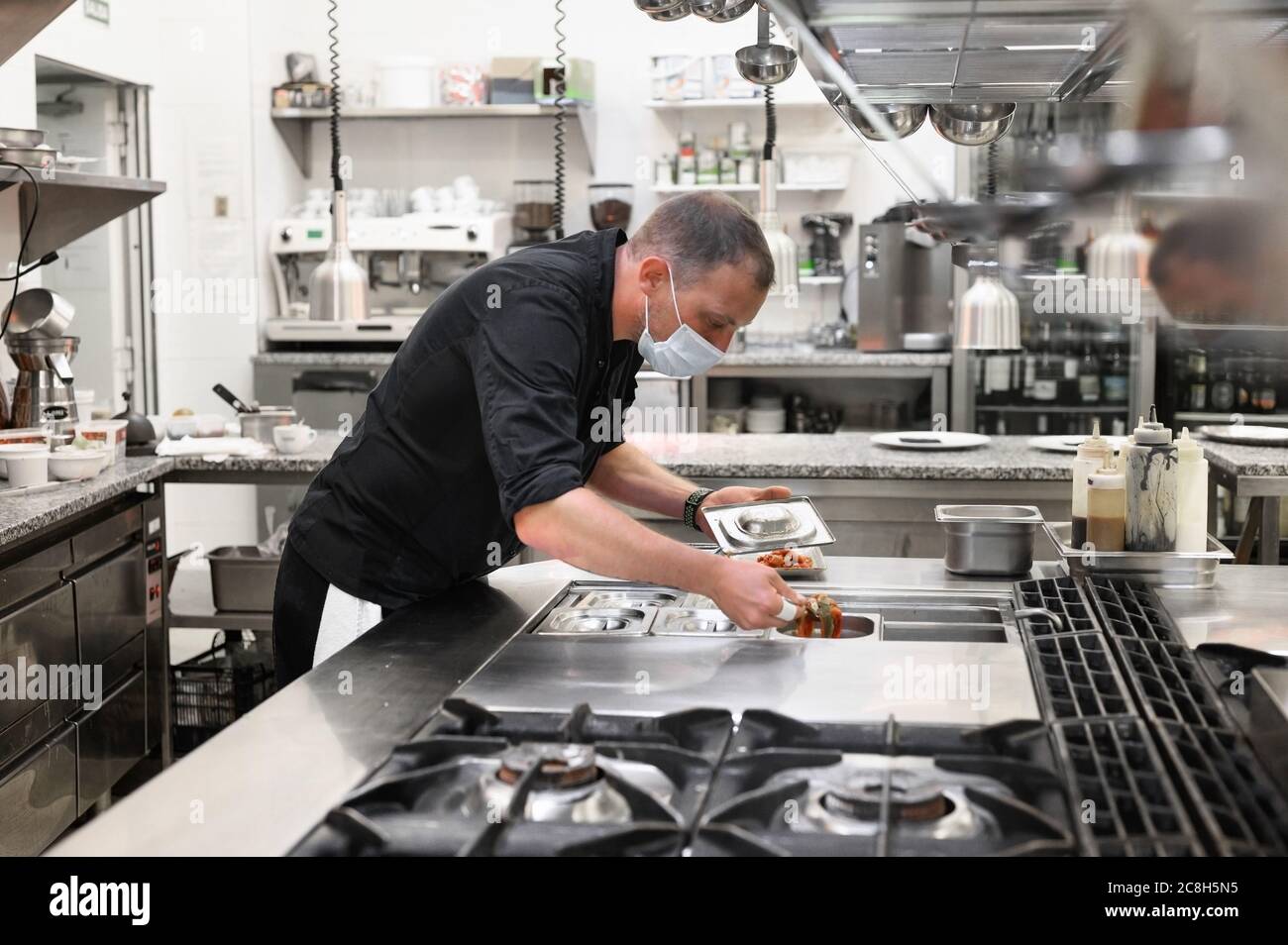 Chef en cuisine uniforme dans une cuisine commerciale. Un cuisinier masculin portant un tablier debout près du comptoir de cuisine préparant les aliments. Photo de haute qualité Banque D'Images
