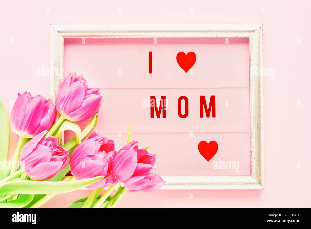 Antécédents de la Fête des mères. J'aime MOM écrit en cadre doré avec des tulipes roses sur fond rose. Vue de dessus. Banque D'Images