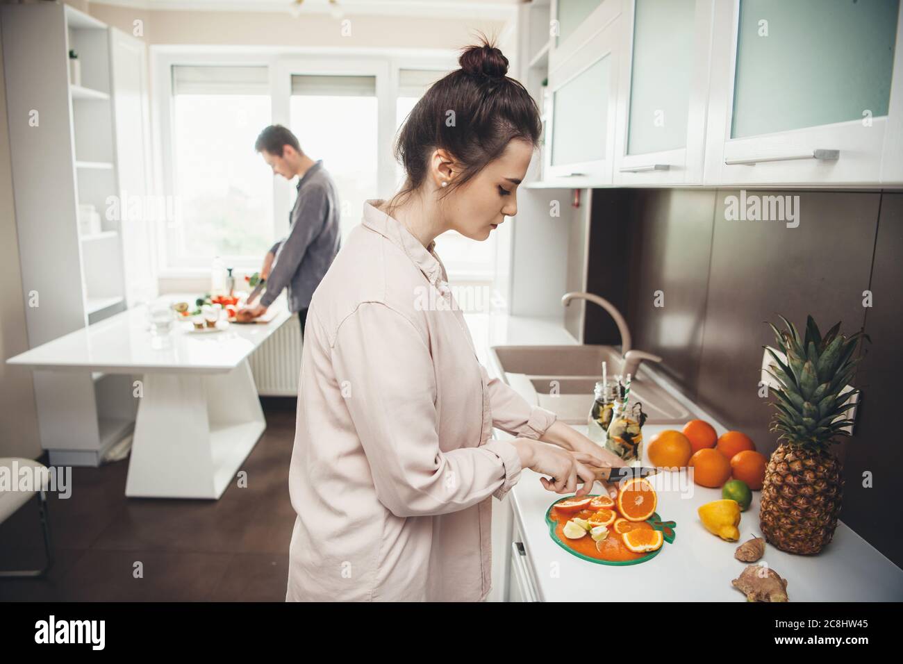 Un jeune couple de caucasiens prépare le petit déjeuner en coupant des fruits dans la cuisine Banque D'Images