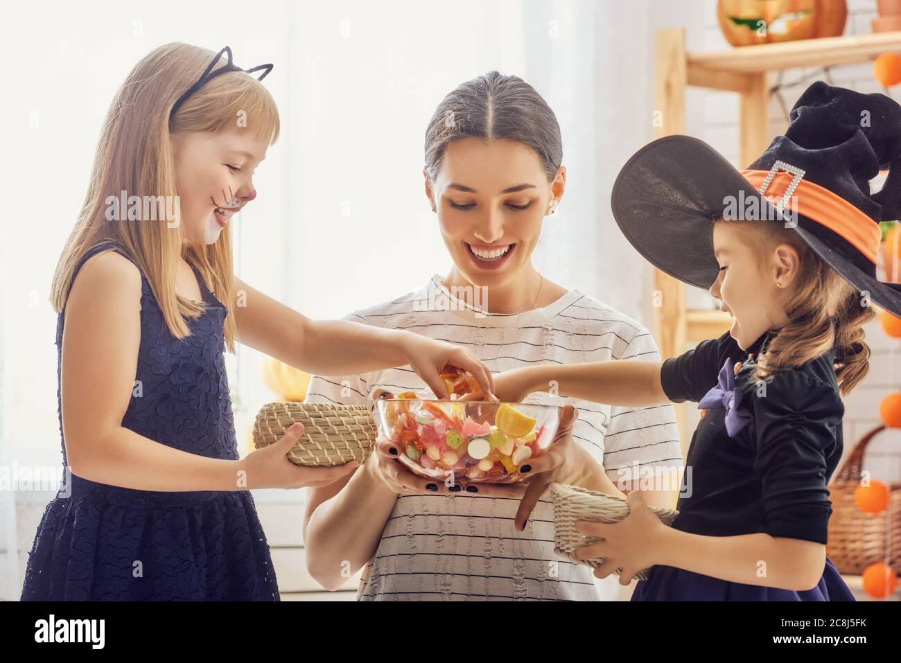 Bonne famille pour Halloween ! Une jeune maman traite les enfants avec des bonbons. Enfants amusants en costumes de carnaval. Banque D'Images