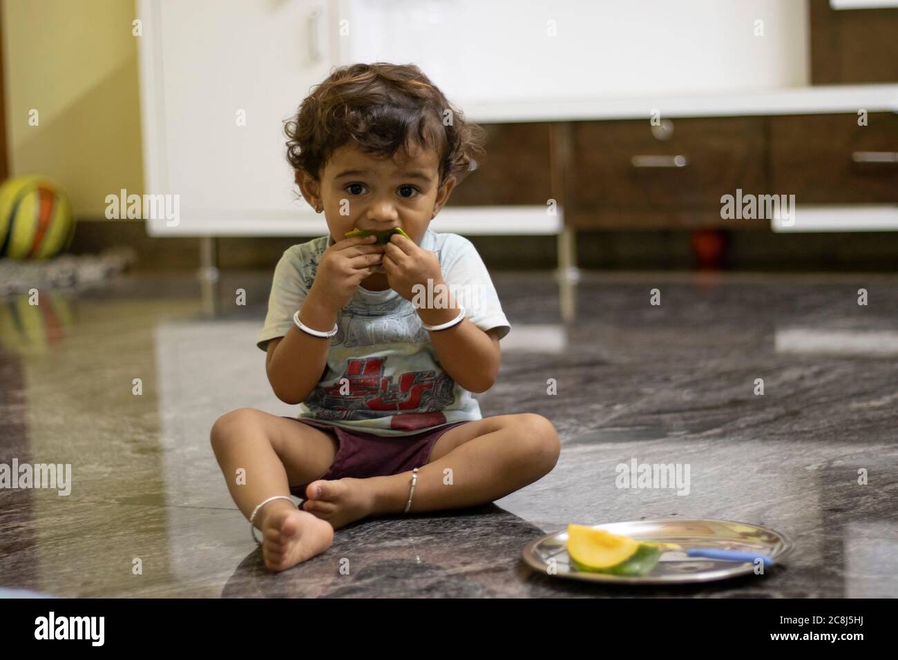 Un petit garçon est assis sur une pierre de marbre mangeant des mangues et gardant des mangues hachées dans une palette près de l'enfant. Banque D'Images