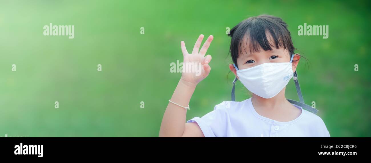 Nouvelle normale :petite fille portant un masque en tissu pour protéger contre la maladie ou la pollution de l'air sa main levée ok posture Banque D'Images