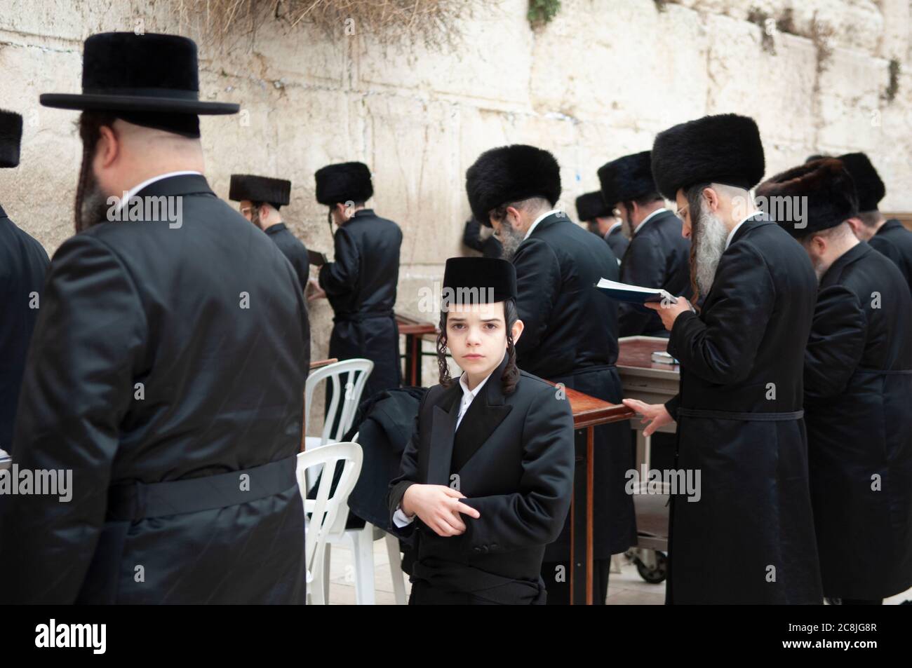 Jérusalem, Israël, mur des lamentations, jeune juif orthodoxe hassidique regardant la caméra entourée de nombreux juifs orthodoxes hassidiques plus anciens au mur des lamentations. Banque D'Images