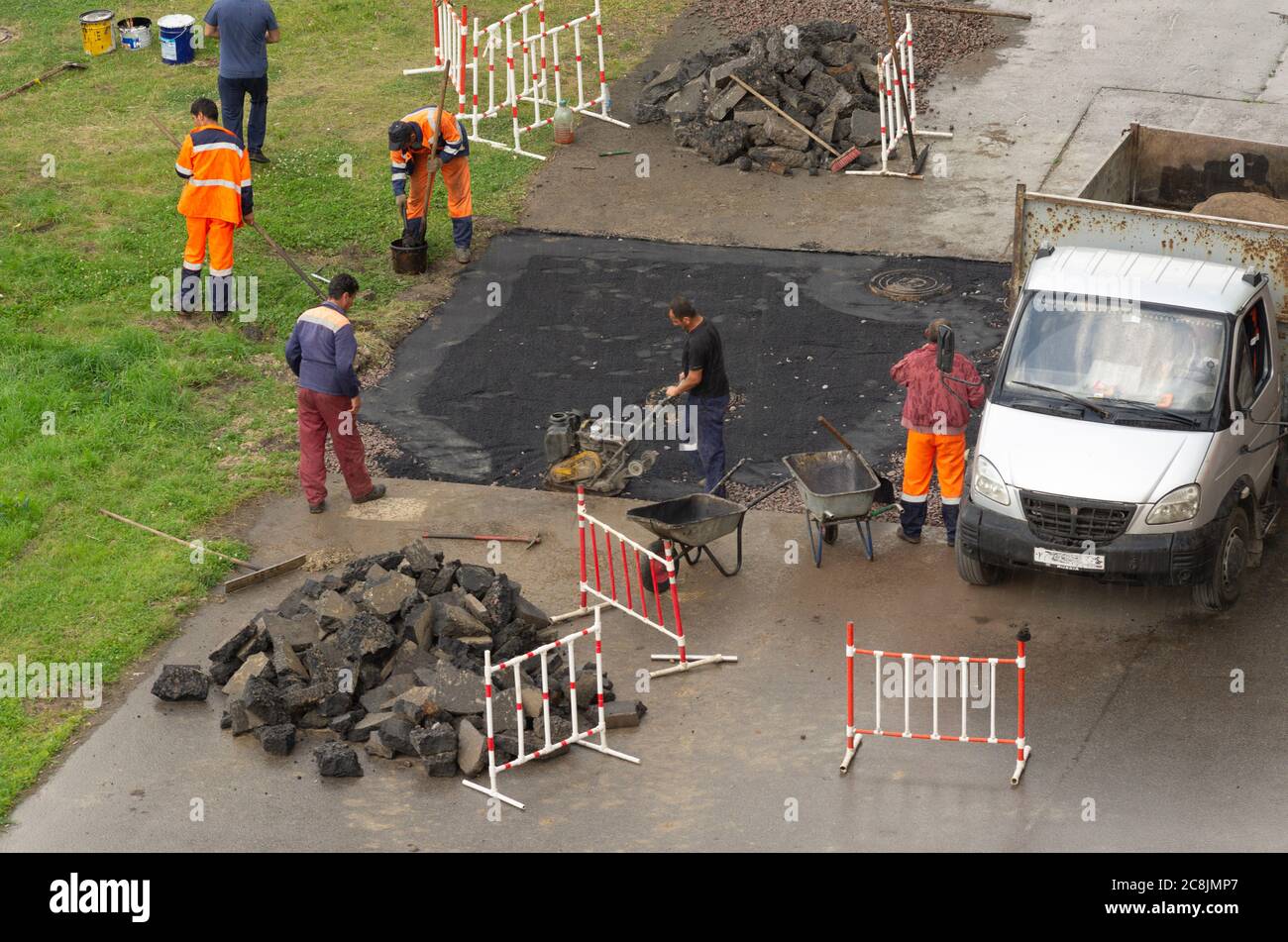 Saint-Pétersbourg, Russie - 28 juillet 2019 : les travailleurs invités en combinaison effectuent des travaux routiers sur la pose d'asphalte par temps pluvieux Banque D'Images