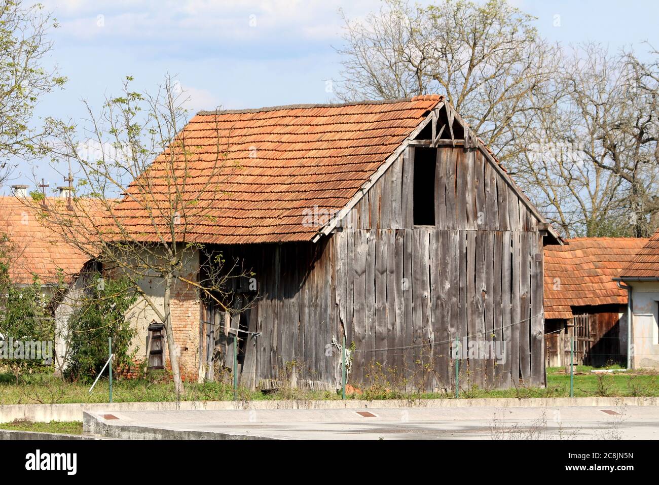 Ancienne grange en bois abandonnée avec des panneaux en bois délabrés cassés et portes détruites à côté de la petite maison familiale et pavés inutilisés parking Banque D'Images Ancienne grange en bois abandonnée avec des panneaux en bois délabrés cassés et portes détruites à côté de la petite maison familiale et pavés inutilisés parking Banque D'Images