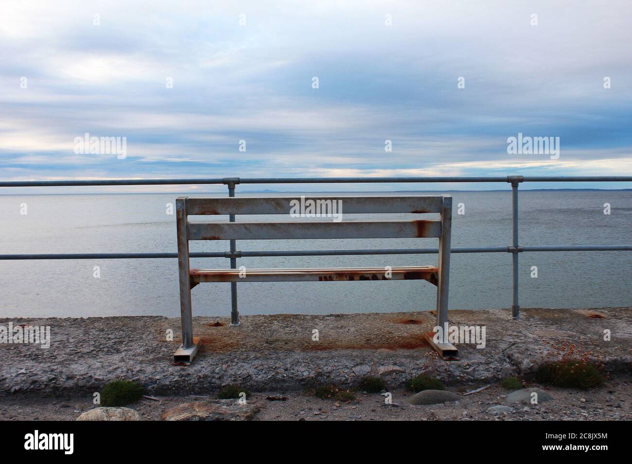 Banc en métal rouillé, avec vue sur les barrières métalliques de la mer d'Irlande au coucher du soleil à Trefor, au nord du pays de Galles Banque D'Images