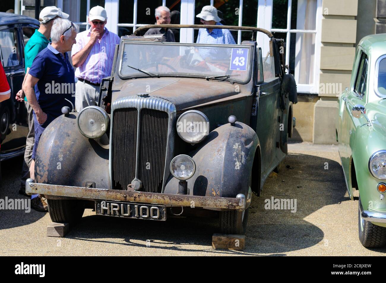 Les hommes qui regardent une grange rouillée et décolorée trouvent une voiture classique à vendre à une vente aux enchères le jour de l'été Banque D'Images