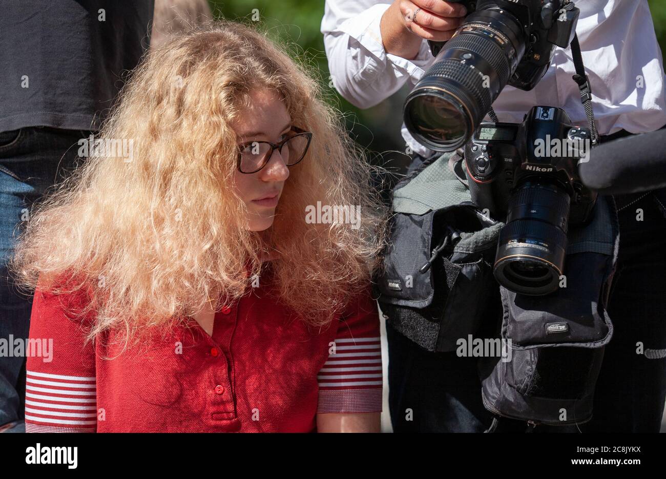 Une jeune femme portant des lunettes se trouve aux appareils photo d'un photographe de presse tandis que les fans et les médias attendent l'arrivée de Johnny Depp devant le tribunal. Banque D'Images