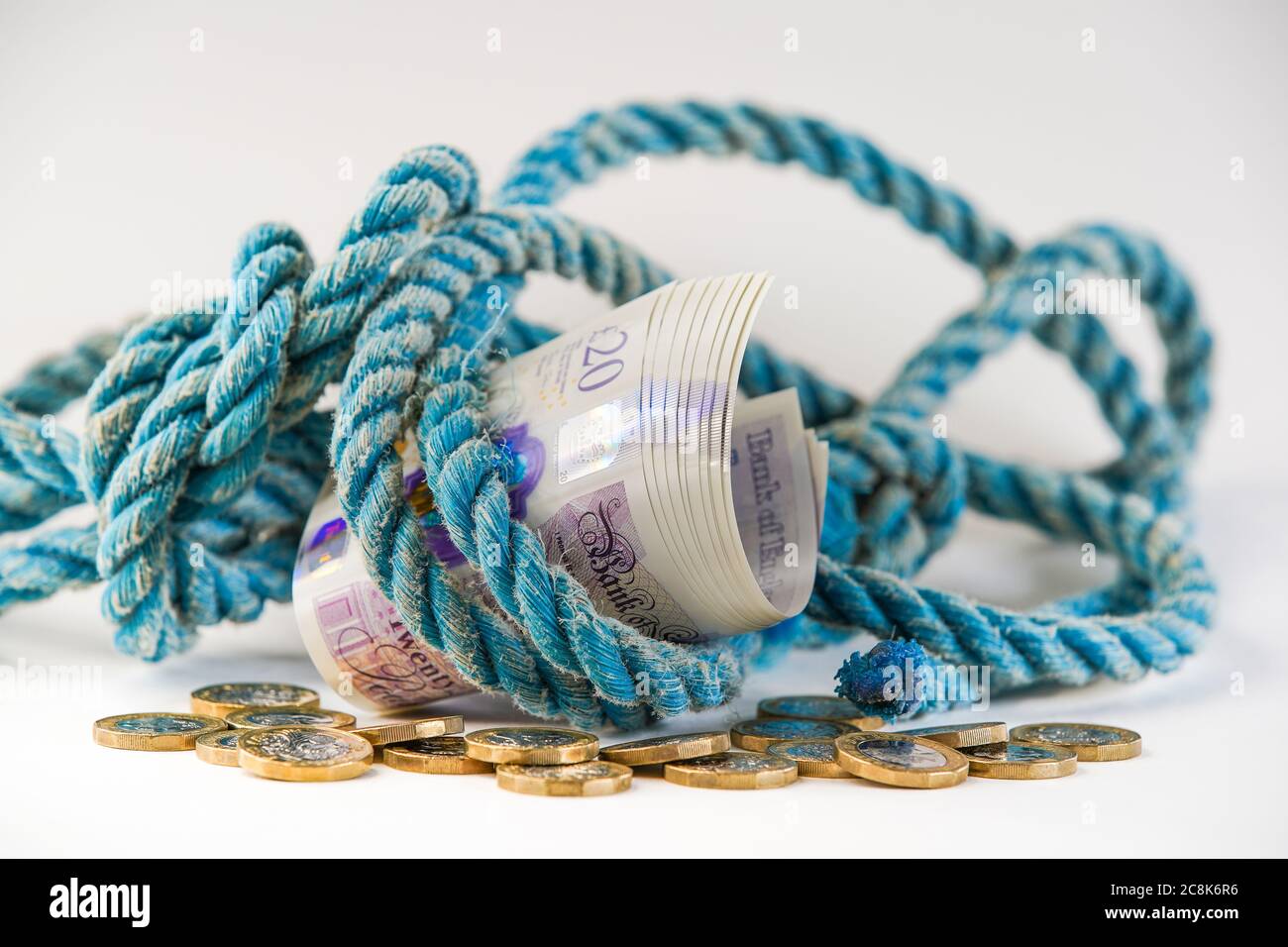Gros plan de £20 notes enveloppées dans une corde ancienne sur une pile de modifications lâches, avec fond blanc.Concept, métaphore: Argent pour vieille corde. Banque D'Images