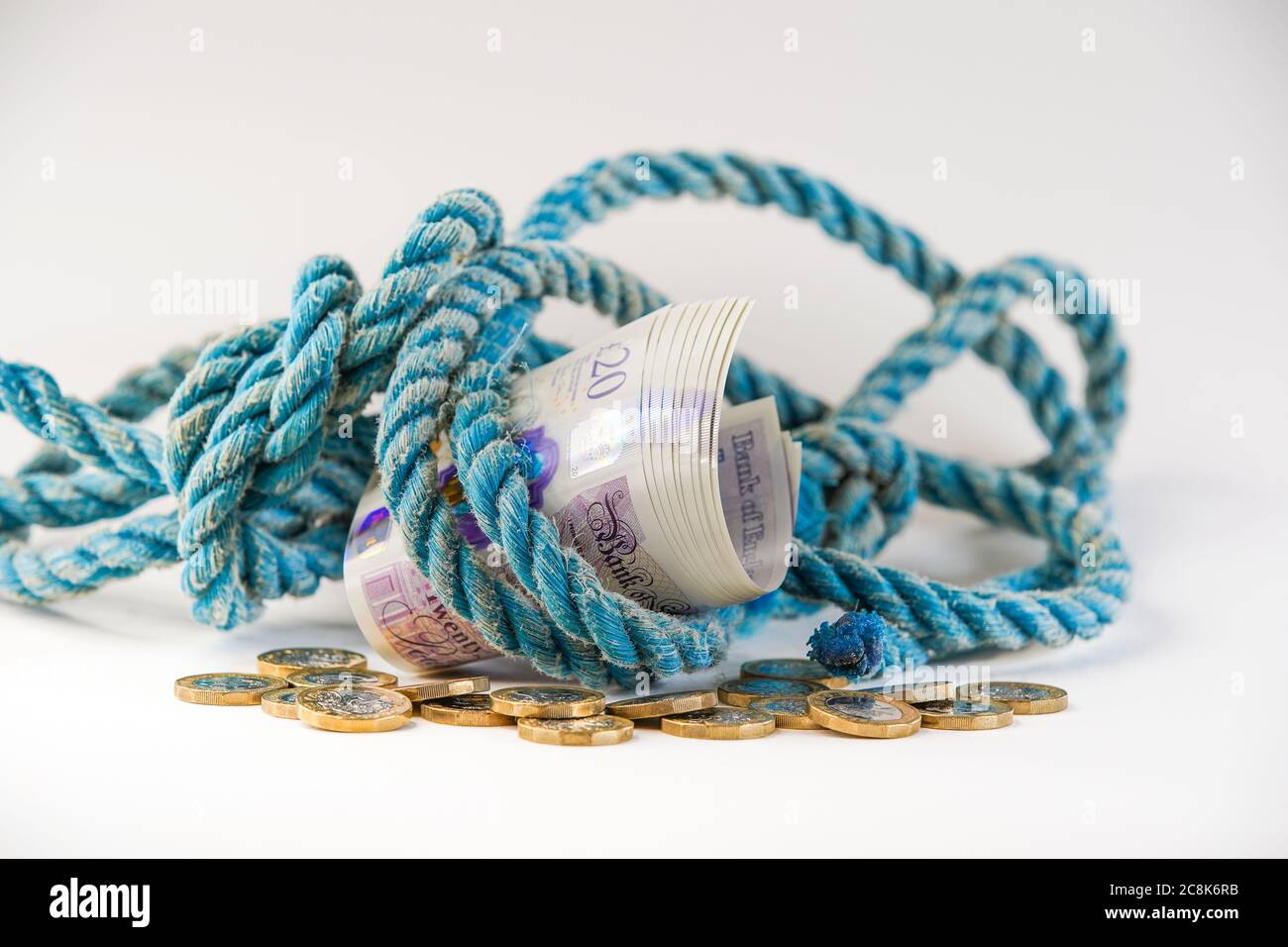 Gros plan d'un paquet de 20 livres sterling de notes enveloppées dans une corde ancienne sur pile de changement lâche, avec fond blanc. Concept, métaphore: Argent pour vieille corde. Banque D'Images