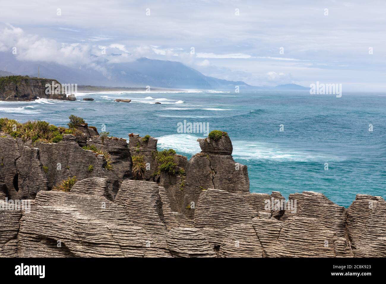 Le célèbre Pancake Rocks sur Dolomite point avec une vue sur la mer vers les montagnes couvertes de nuages. Dolomite point, Île du Sud, Nouvelle-Zélande Banque D'Images