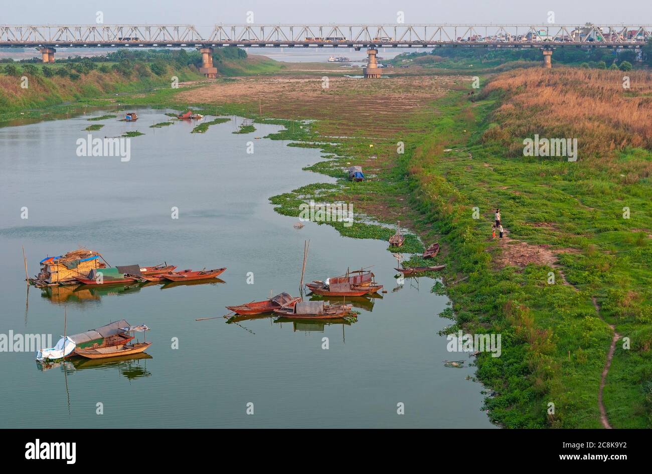 Long pont de Bien au coucher du soleil par la rivière rouge avec des bateaux de pêche, Hanoi, Nord Vietnam. Banque D'Images