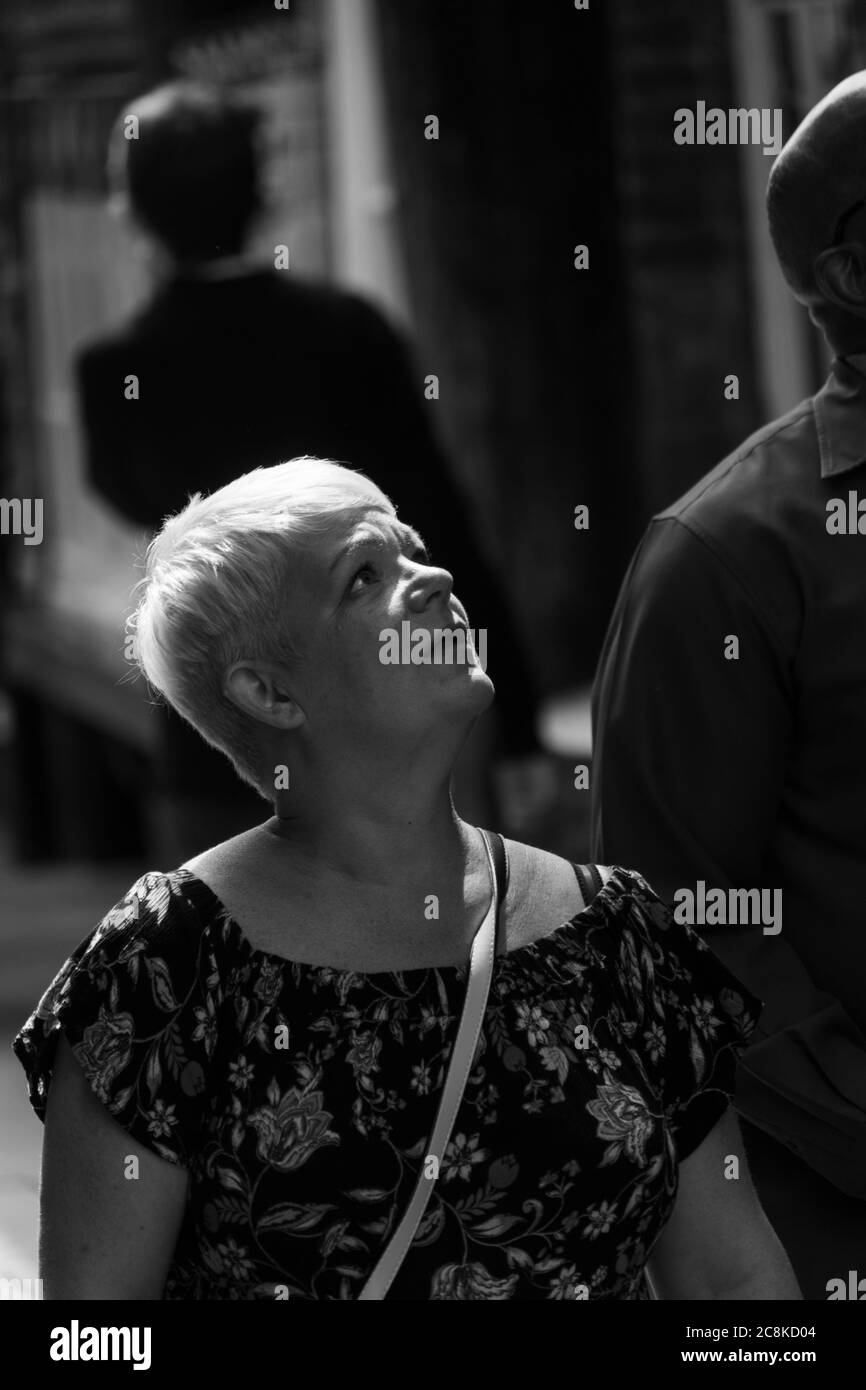Femme blonde marchant dans une rue de ville avec le soleil brille sur son visage, York, North Yorkshire, Angleterre, Royaume-Uni. Banque D'Images