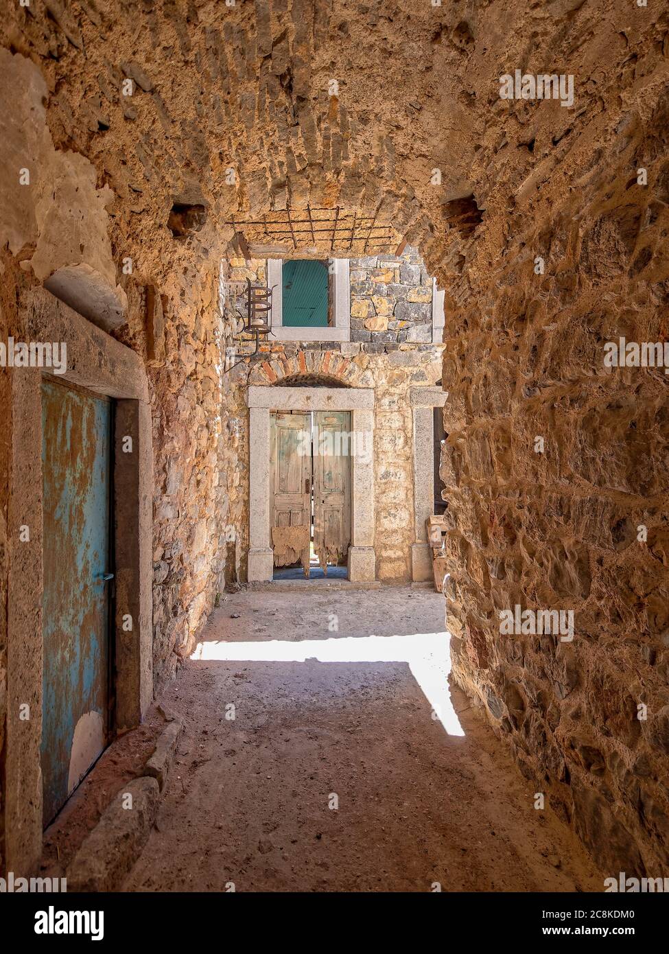 Entouré de pierre. Une petite tache de soleil éblouissante et une porte abîmé au bout d'une allée voûtée dans la ville médiévale de Pyrgi, île de Chios, Grèce. Banque D'Images