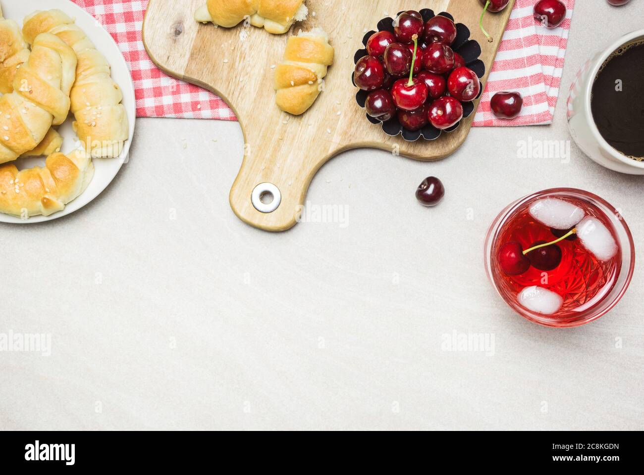 Petit-déjeuner avec croissants faits maison, café, jus de fruits et cerises douces sur fond texturé clair, vue de dessus avec photocopieuse. Banque D'Images