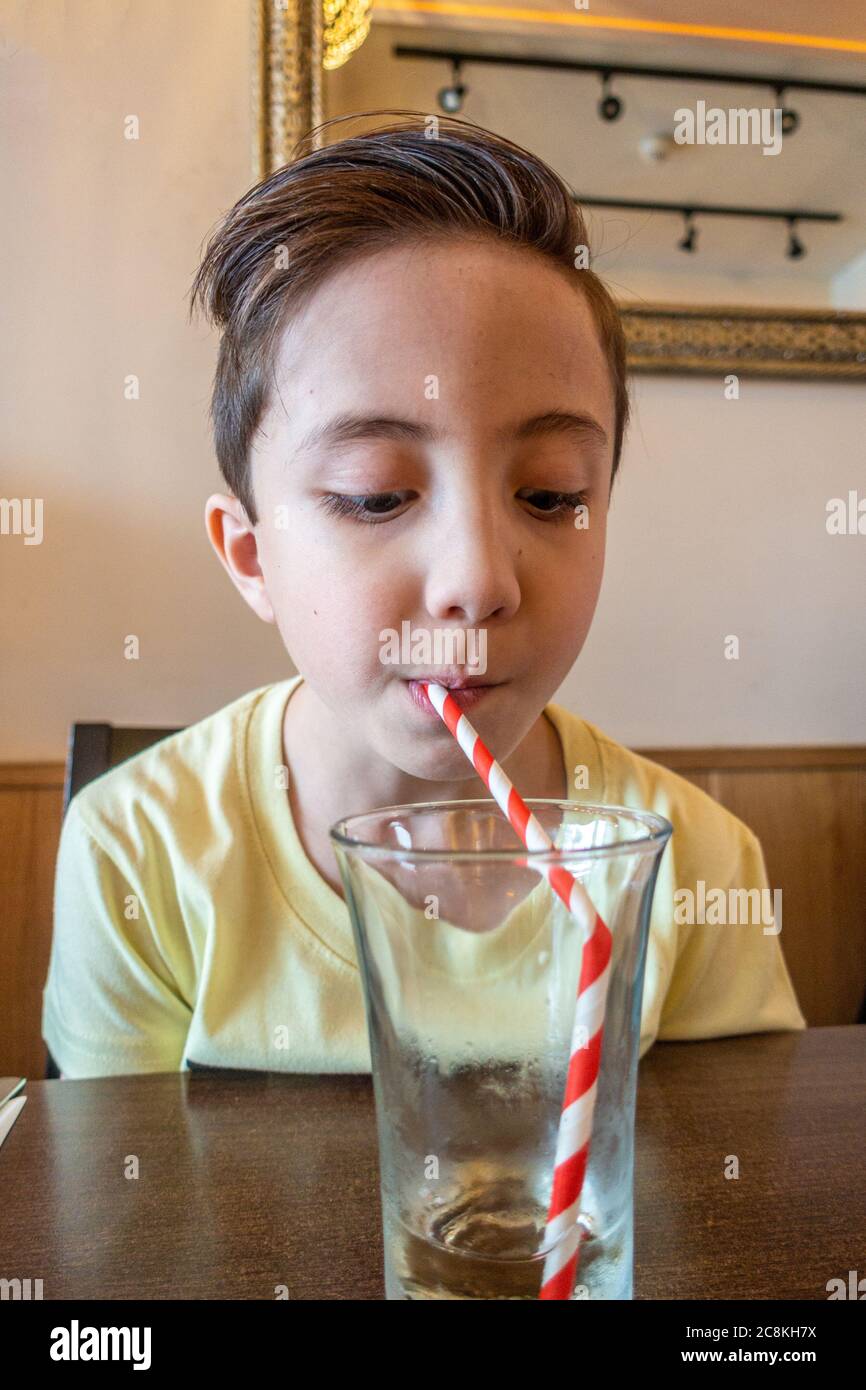 Un jeune garçon a fini de boire un verre avec une paille de papier. Banque D'Images