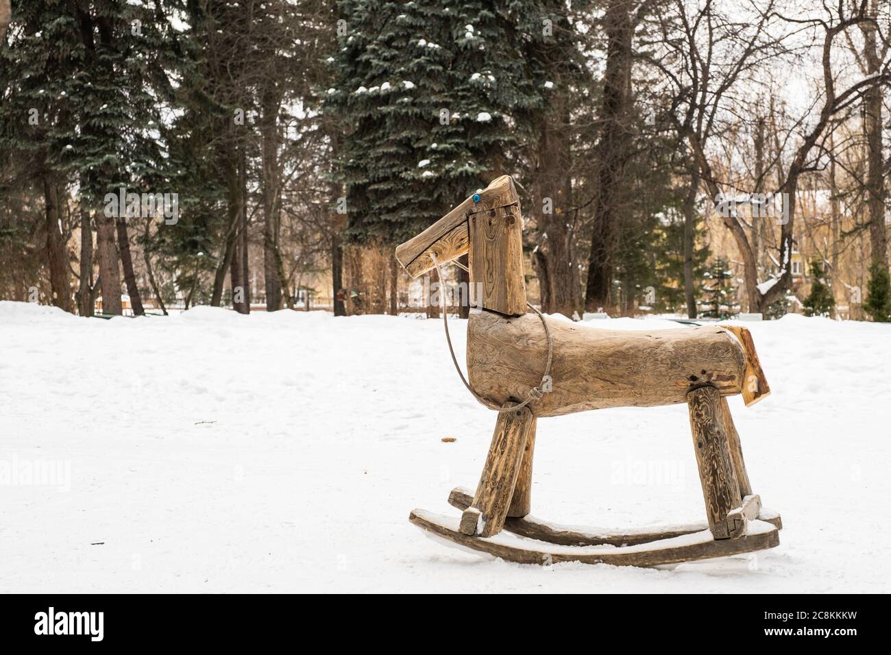 Paysage d'hiver. Un petit balancement en bois pour enfants - un joli cheval dans un clairière sur fond de neige blanche et d'arbres dans un parc de la ville. Banque D'Images