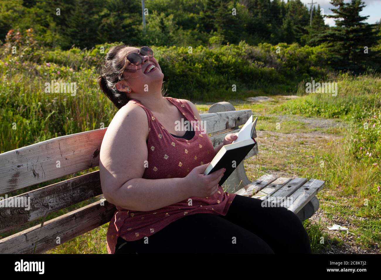 Une femme s'ébaise en lisant son livre à l'extérieur sur un banc de parc Banque D'Images