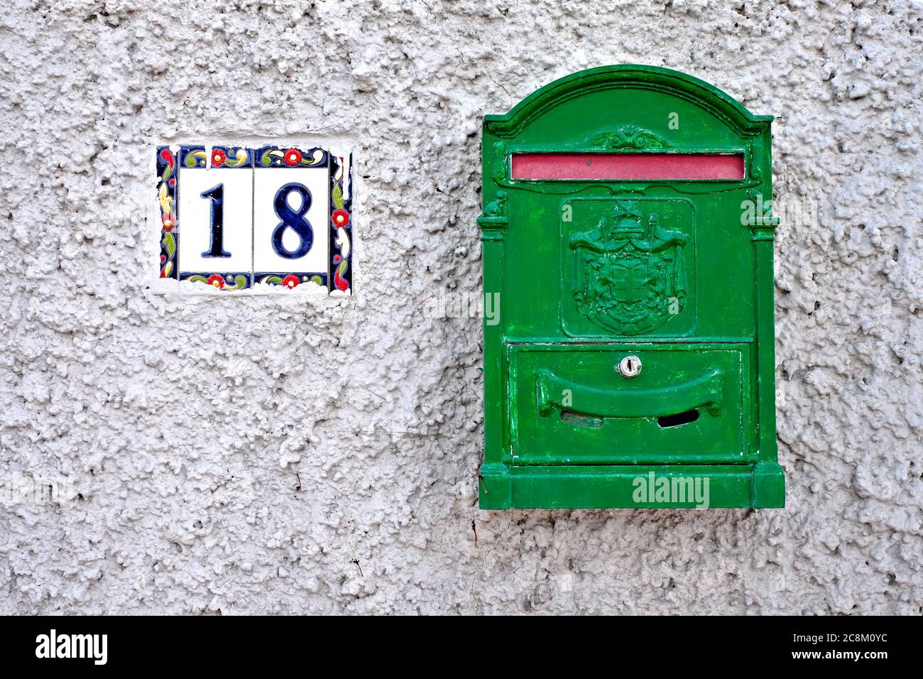 Une boîte de lettres verte et le chiffre 18 sur un mur gris. Banque D'Images