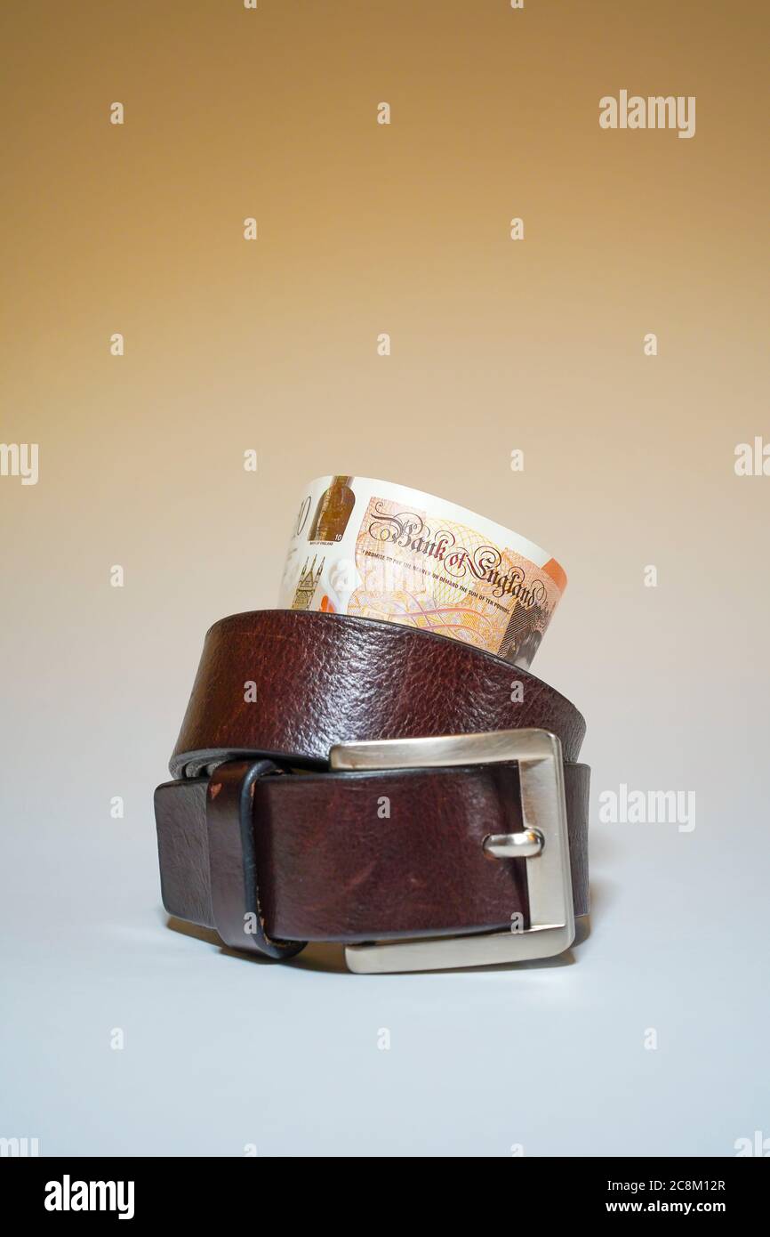 Paquet de notes britanniques de dix livres à l'intérieur d'une ceinture de serrage sur fond blanc. Métaphore, concept: Serrer la ceinture, dépenser moins d'argent, budgétisation. Banque D'Images