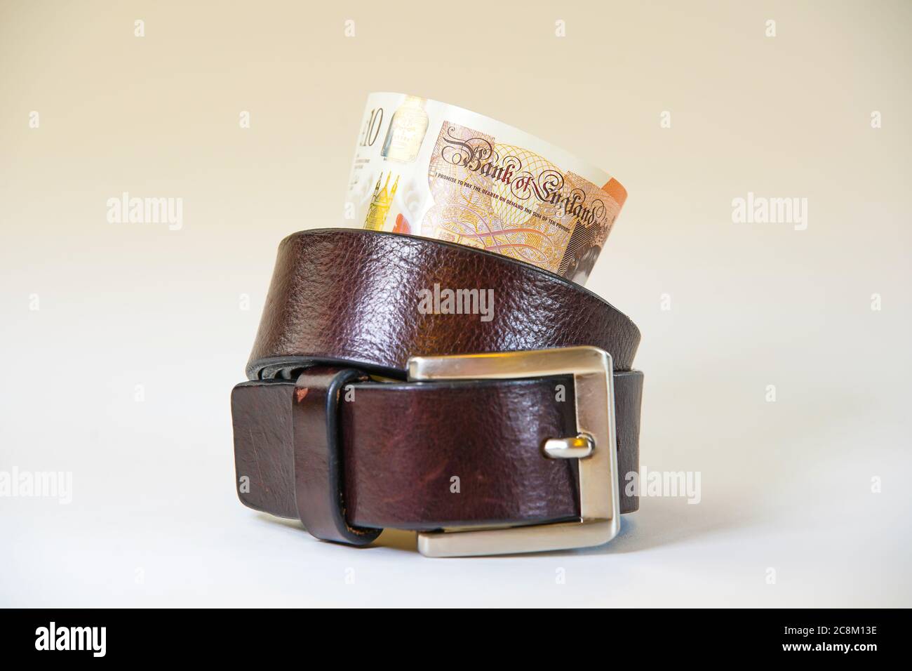 Des notes britanniques de dix livres à l'intérieur d'une ceinture de serrage sur fond blanc. Métaphore, concept: Serrer la ceinture, dépenser moins d'argent, budgétisation. Banque D'Images