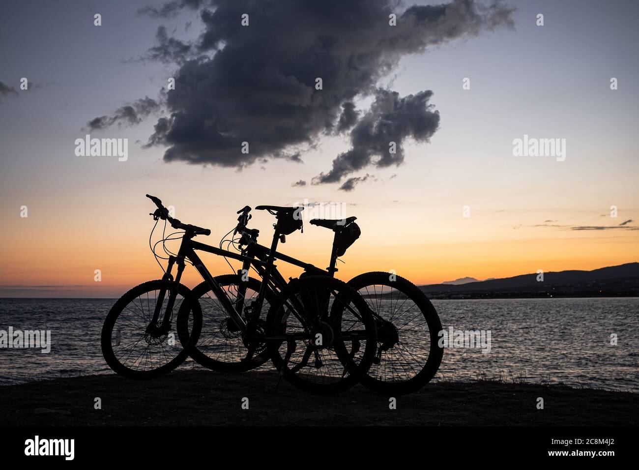 Deux VTT se tiennent au bord d'une falaise, où vous pouvez voir un coucher de soleil orange vif sur la mer, des montagnes et de grands nuages. Loisirs et sports Banque D'Images