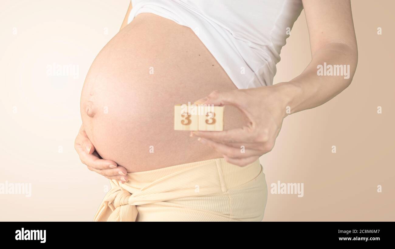 Jeune femme enceinte avec numéro de semaine de grossesse à côté de son ventre. Photos de la croissance du ventre à 33 semaines de grossesse. Alimentation saine pendant la grossesse Banque D'Images