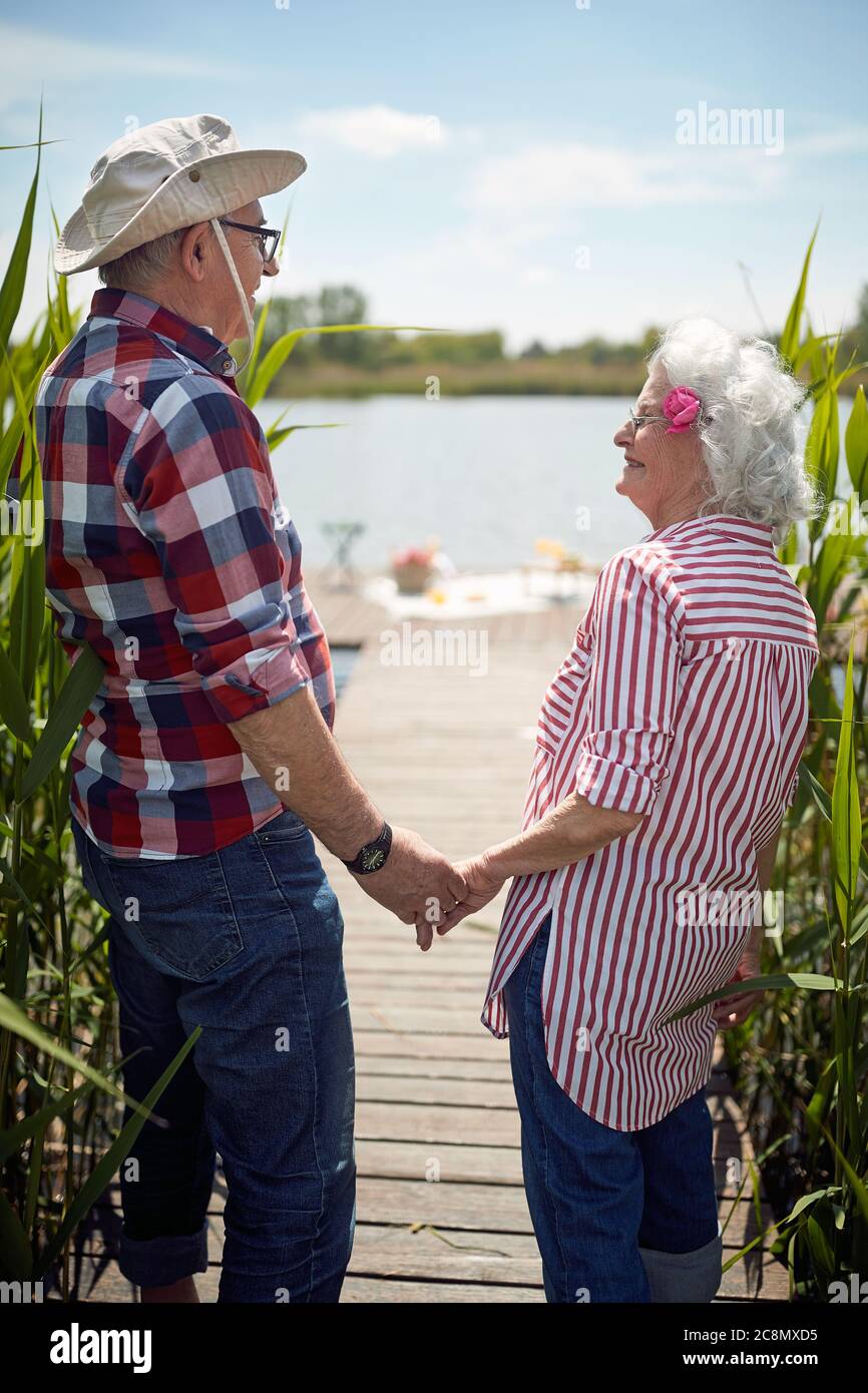gros plan de couple caucasien vieux tenant les mains, regardant l'un l'autre, souriant, debout au bord du lac Banque D'Images