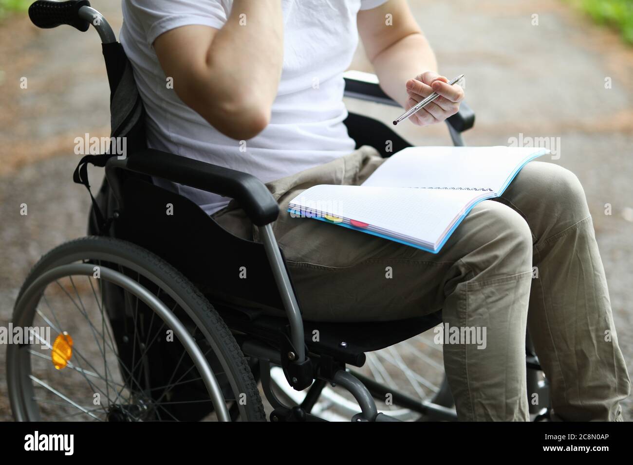 Homme assis en fauteuil roulant et prendre note dans le carnet dans le parc. Banque D'Images