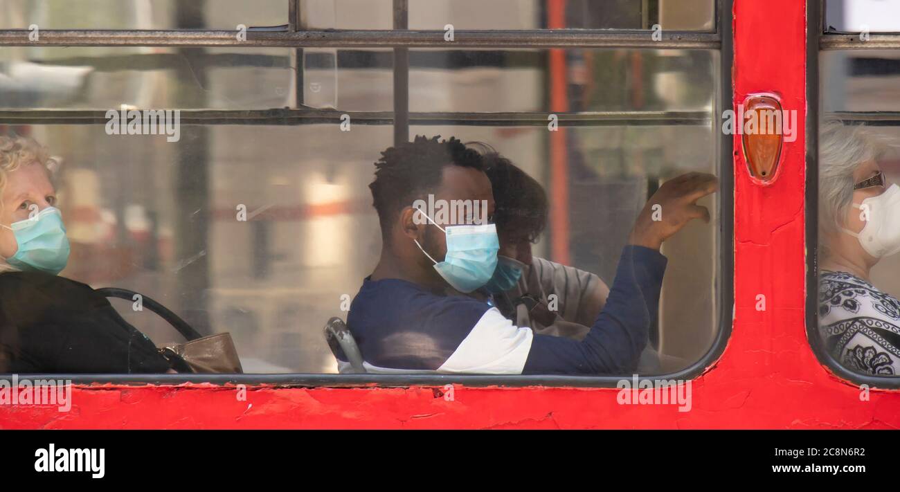Belgrade, Serbie - 16 juillet 2020 : jeune homme noir portant un masque chirurgical tout en étant assis et en montant sur un siège de fenêtre d'un tramway Banque D'Images