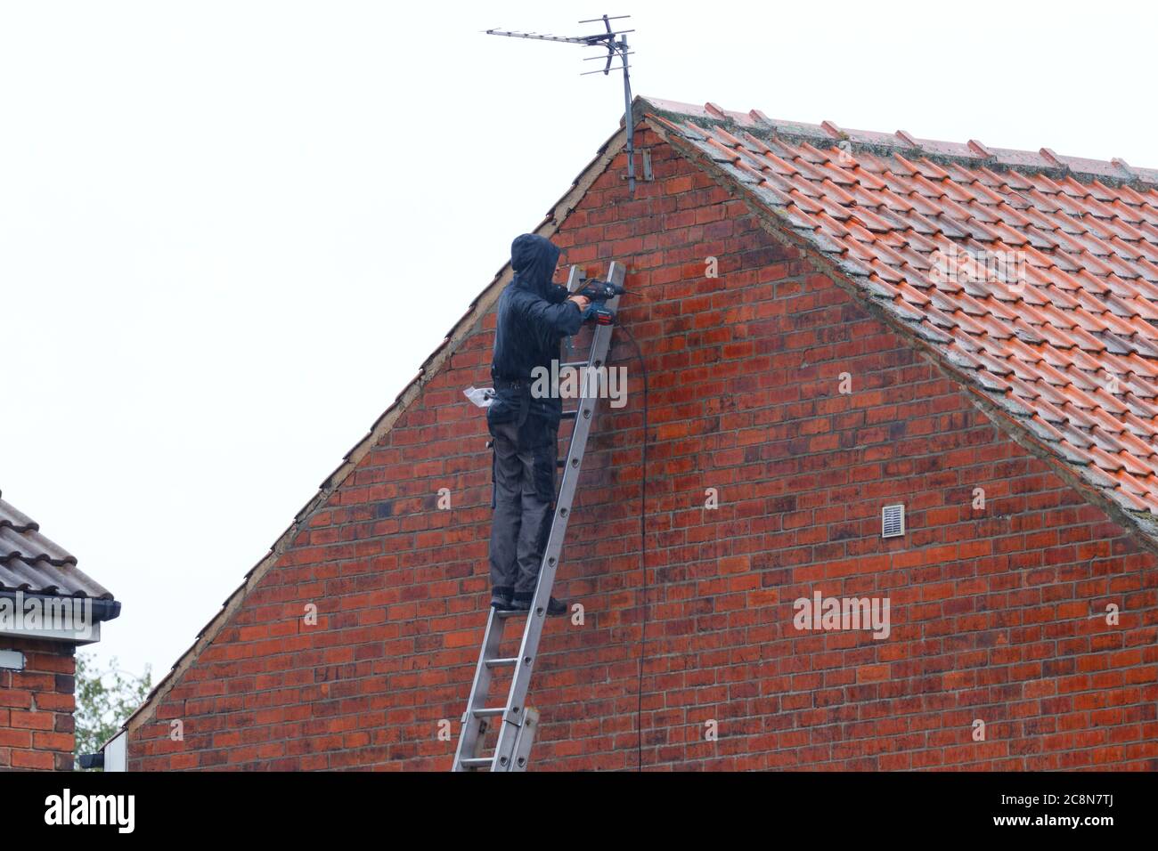 Un homme installant une antenne tv sur une maison, pendant qu'il pleut. Banque D'Images