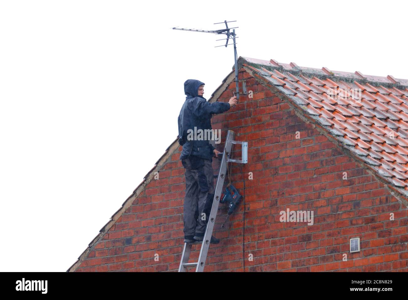 Un homme installant une antenne tv sur une maison, pendant qu'il pleut. Banque D'Images