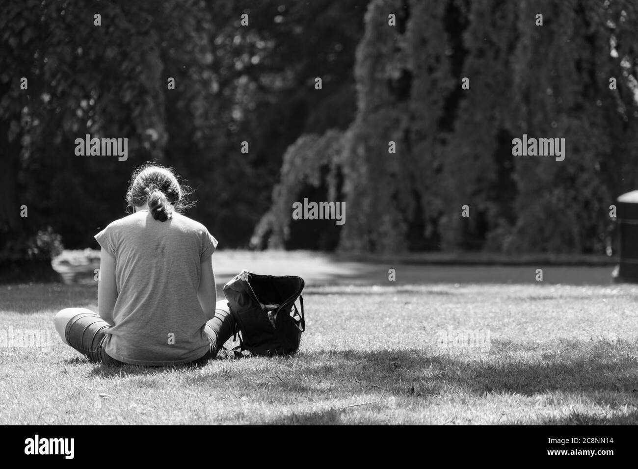 Une femme assise sur l'herbe dans un parc lors d'une matinée ensoleillée au cours d'un lock-up, les jardins de la vallée, Harrogate, North Yorkshire, Angleterre,Royaume-Uni. Banque D'Images