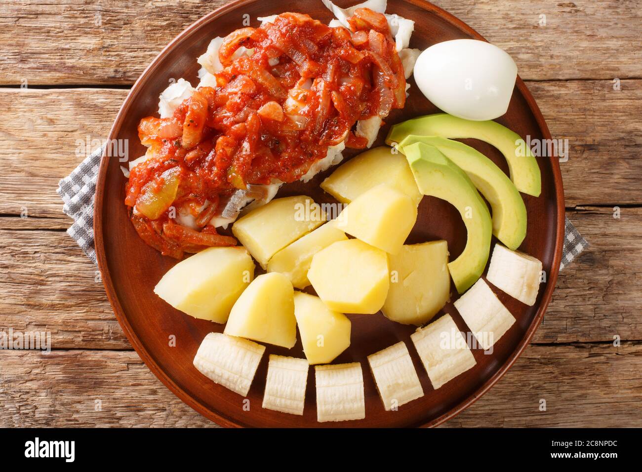 Petit déjeuner au morue des Bermudes avec sauce tomate à l'oignon, pommes de terre bouillies, œufs, banane et avocat dans une assiette sur la table. Vue horizontale sur le dessus Banque D'Images