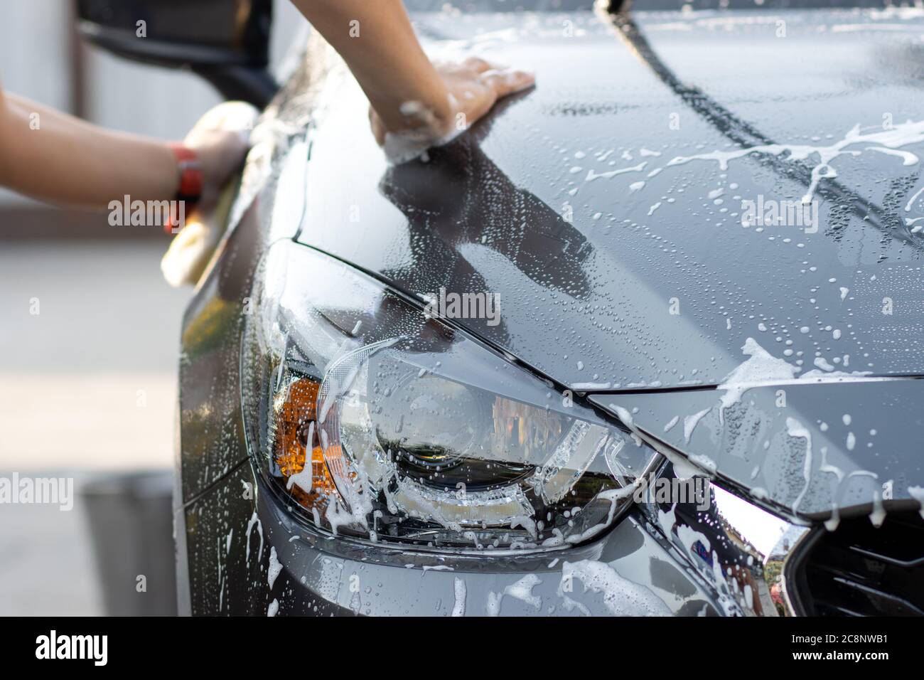 Laver la voiture à la main à l'eau savonneuse. L'homme nettoie la voiture avec une éponge, de l'eau et du détergent. Banque D'Images