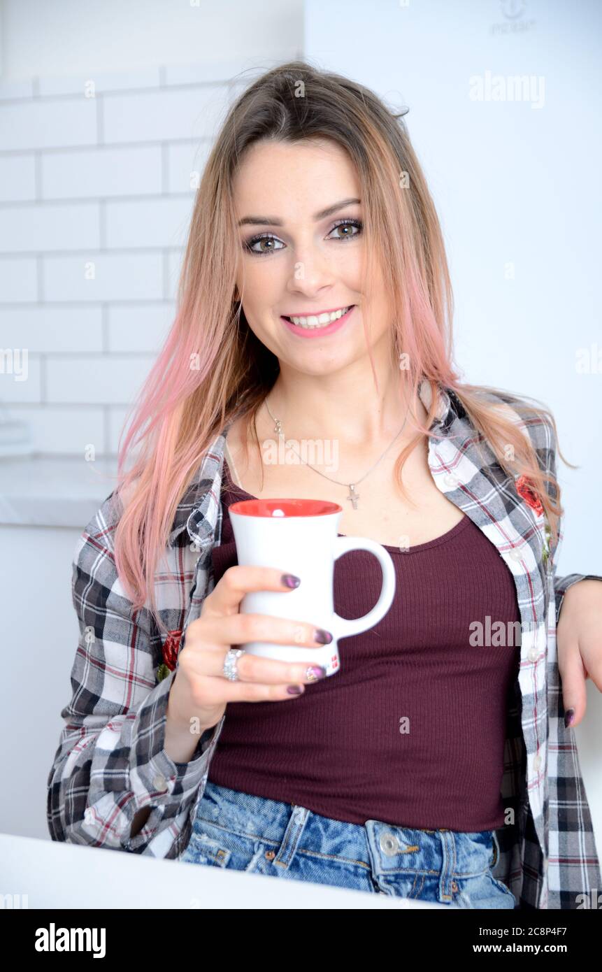 Fille polonaise souriante, couleur des poils mélangés. Jeune femme tenant une tasse blanche et appréciant sa boisson. Banque D'Images