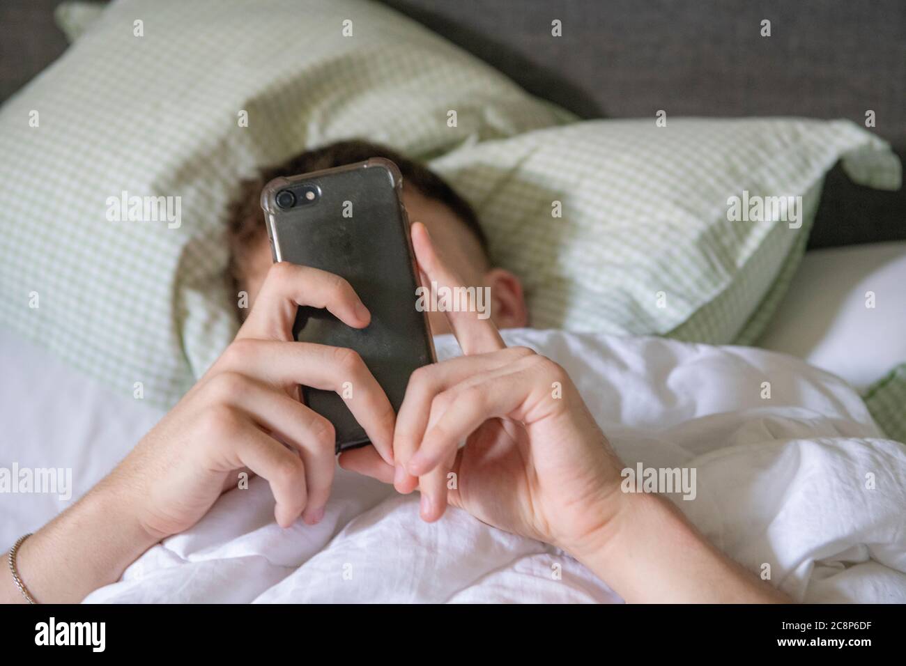 Un jeune garçon est au lit avec son téléphone portable Banque D'Images