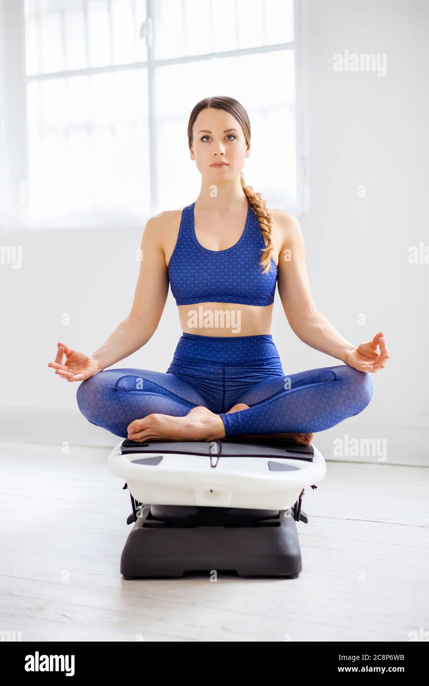 Jeune femme méditant dans la position lotus sur une surfset dans une salle de gym de haute clé dans un concept de santé et de forme physique ou bien-être Banque D'Images