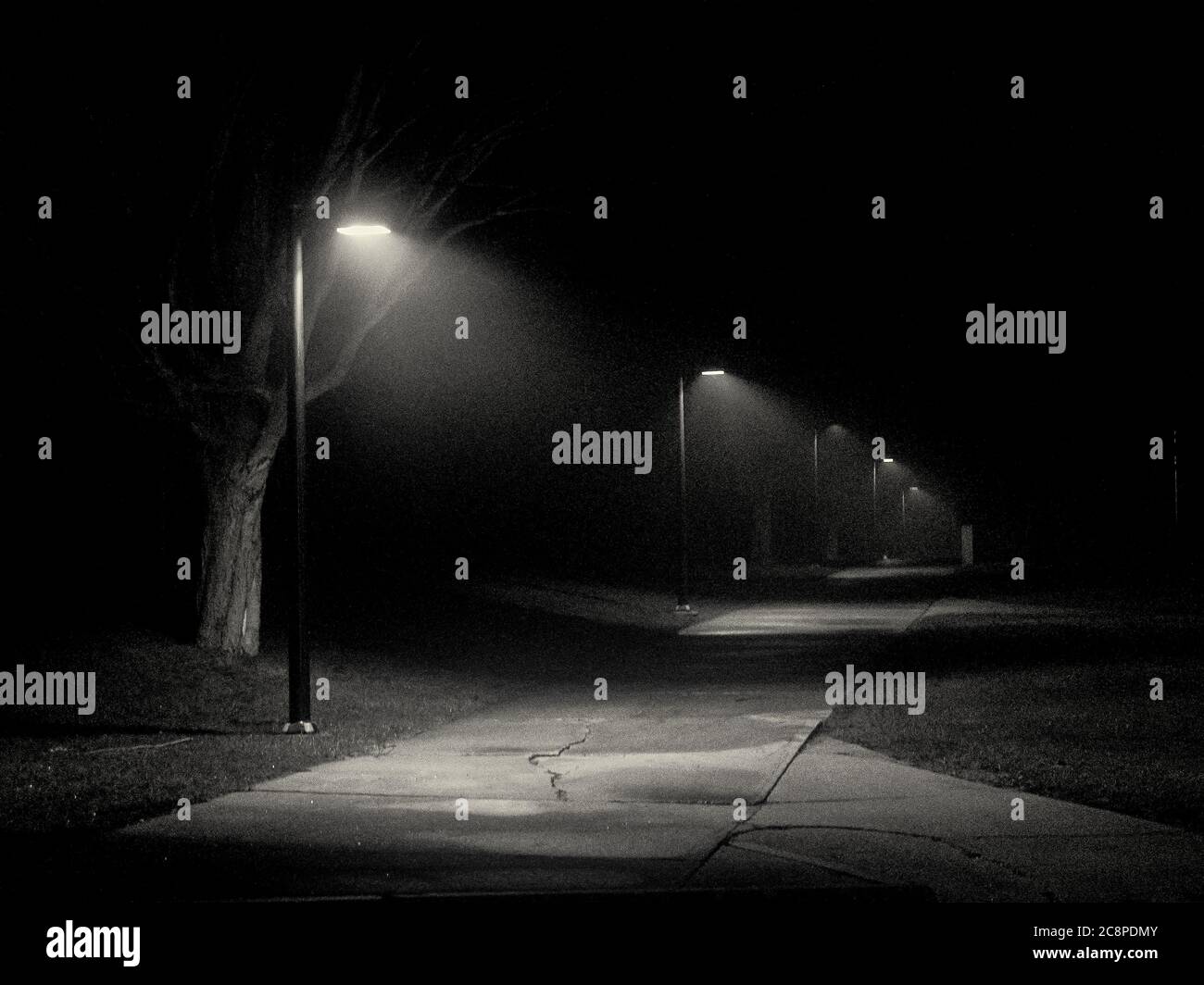 Un trottoir éclairé par des lumières en noir et blanc la nuit Banque D'Images