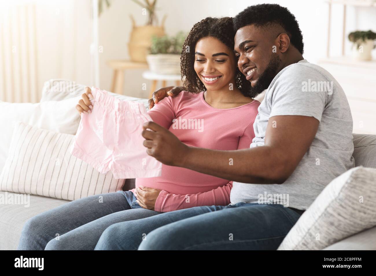 Noir souriant s'attendant à un couple tenant des vêtements de bébé Banque D'Images